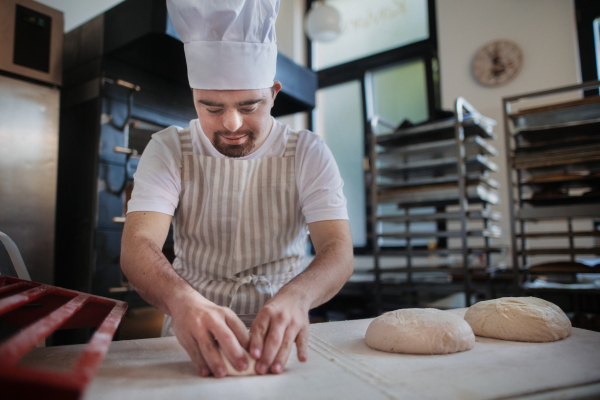 Young baker with down syndrome preparing pastries in bakery. Concept of integration people with a disabilities into society.