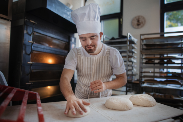 Young baker with down syndrome preparing pastries in bakery. Concept of integration people with a disabilities into society.