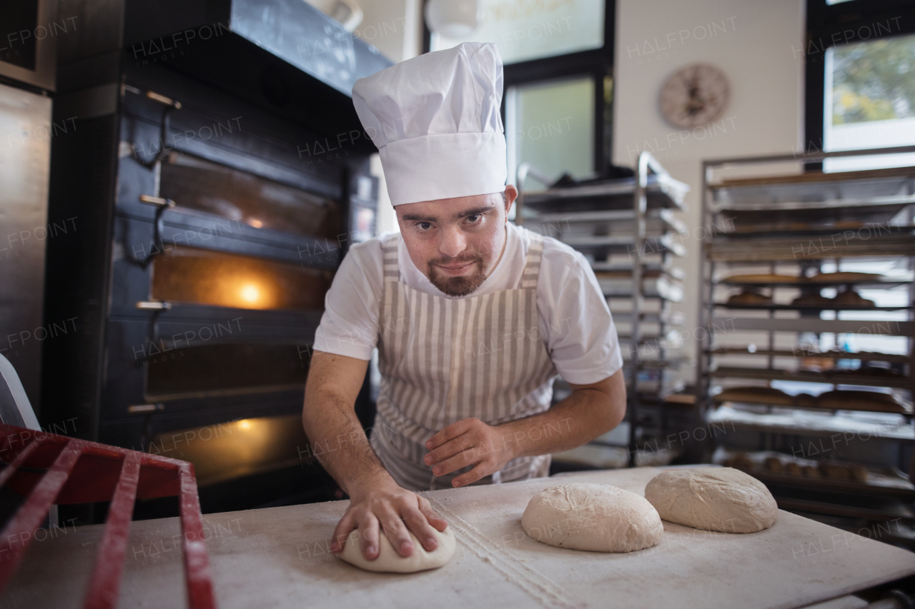 Young baker with down syndrome preparing pastries in bakery. Concept of integration people with a disabilities into society.