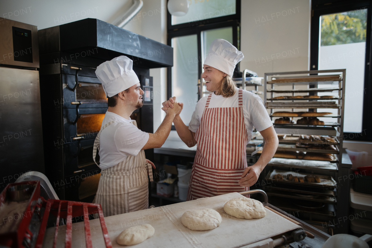 Man with down syndrom helping prepair bread in a bakery with his colleague. Concept of integration people with disability into society.