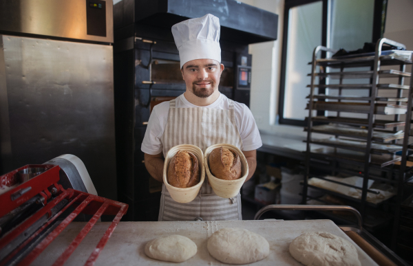 Young baker with down syndrome preparing pastries in bakery. Concept of integration people with a disabilities into society.