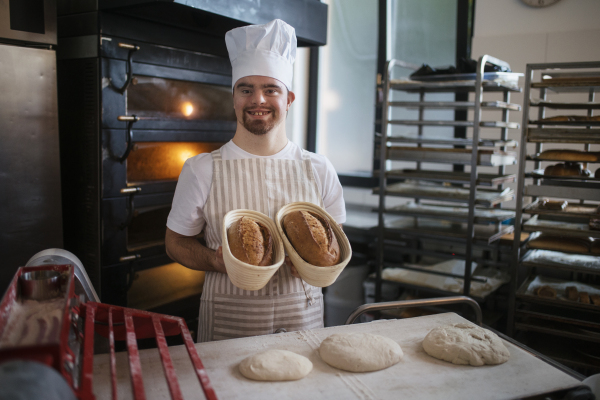 Young baker with down syndrome preparing pastries in bakery. Concept of integration people with a disabilities into society.