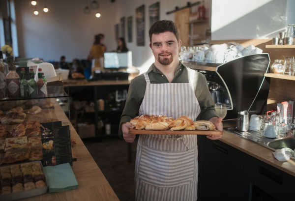 Man with down syndrom working in cafe, carring fresh pastries. Concept of integration people with a disabilities into society.