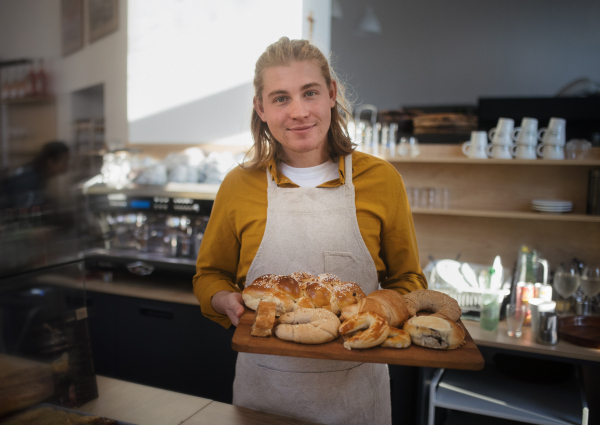 Young man working in a cafe, carring fresh pastries.