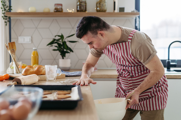 Young man with Down syndrome baking cookies at home. Everyday routine for man with Down syndrome genetic disorder.