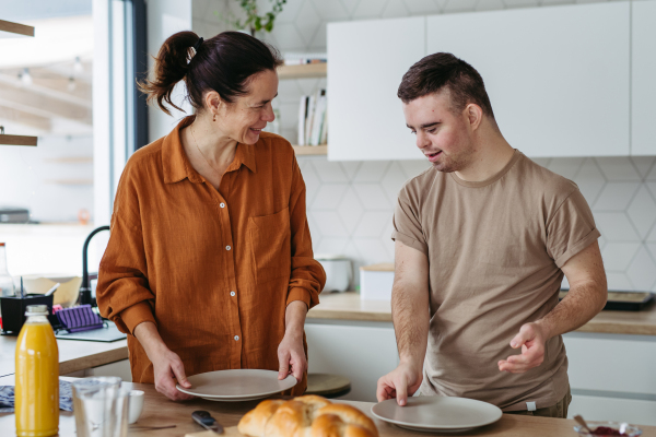 Young man with Down syndrome preparing breakfast with his mother at home. Morning routine for man with Down syndrome genetic disorder.