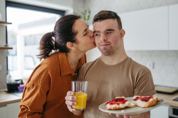 Portrait of young man with Down syndrome serving breakfast to his mother as a Mother's Day gift. Concept of Mother's Day and maternal love to disabled children.