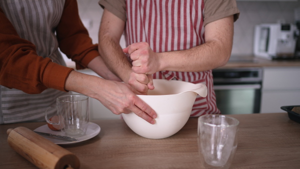 A close up of young man with Down syndrome preparig dough for cookies with his mom at home. Everyday routine for man with Down syndrome.