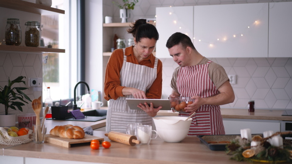 A young man with Down syndrome preparig dough for cookies with his mom at home. Everyday routine for man with Down syndrome.