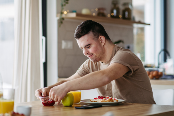 Young man with Down syndrome preparing breakfast on his own. Morning routine for man with Down syndrome genetic disorder.