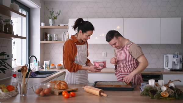 Young man with Down syndrome baking cookies with his mom at home. Everyday routine for man with Down syndrome genetic disorder.