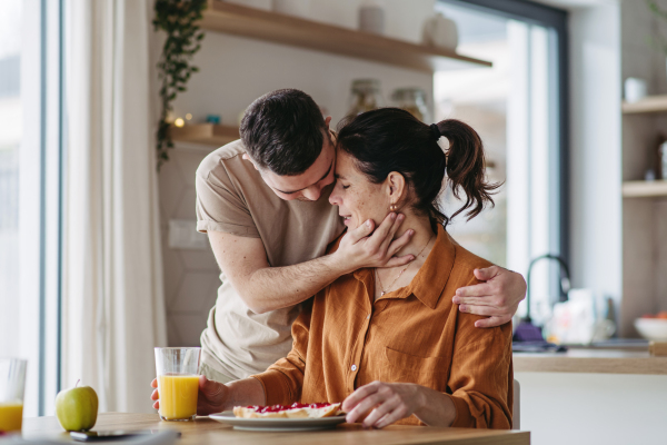 Portrait of young man with Down syndrome serving breakfast to his mother as a Mother's Day gift. Concept of Mother's Day and maternal love to disabled children.