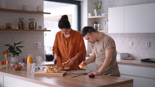 Young man with Down syndrome preparing breakfast with his mother at home. Morning routine for man with Down syndrome genetic disorder.