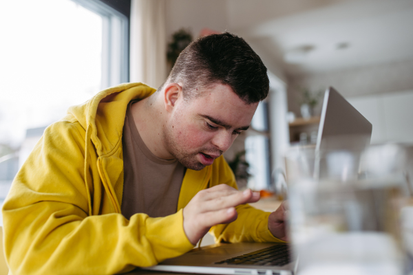 Young man with down syndrome learning online at home, using laptop, working on notebook. Telehealth consultation with doctor.