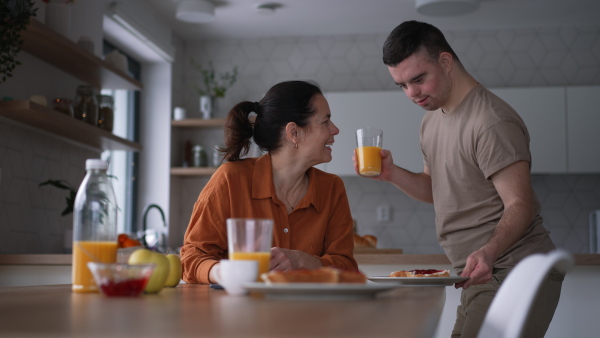 Young man with Down syndrome preparing breakfast with his mother at home. Morning routine for man with Down syndrome genetic disorder.