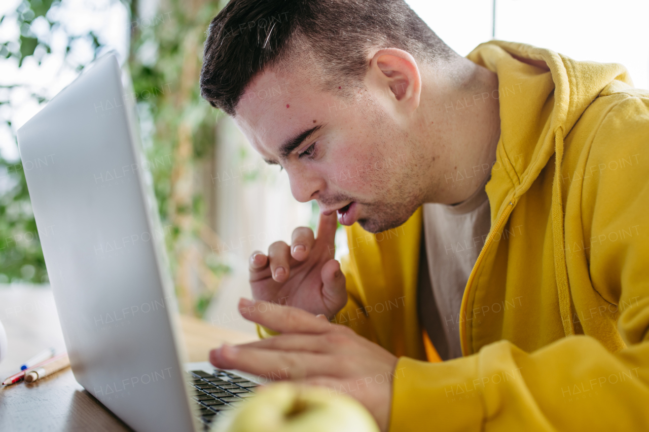 Young man with down syndrome learning online at home, using laptop, working on notebook. Telehealth consultation with doctor.