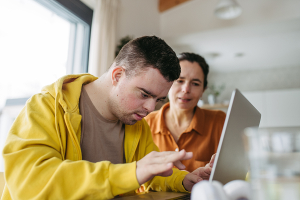 Mom teaching a young man with down syndrome, using laptop. Telehealth consultation with doctor.