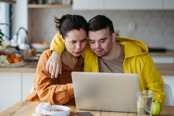 Mom teaching a young man with down syndrome, using laptop. Telehealth consultation with doctor.