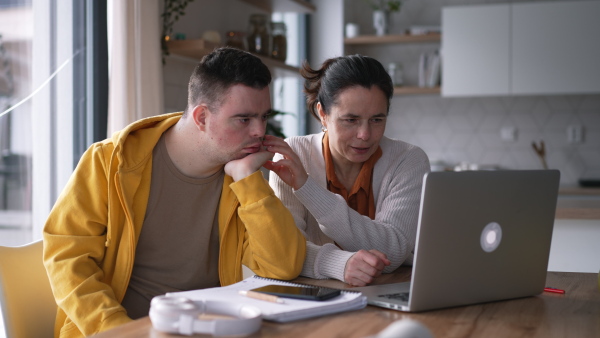 Mom teaching a young man with down syndrome, using laptop. Telehealth consultation with doctor.