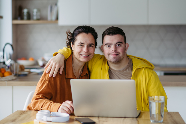 Mom teaching a young man with down syndrome, using laptop. Telehealth consultation with doctor.