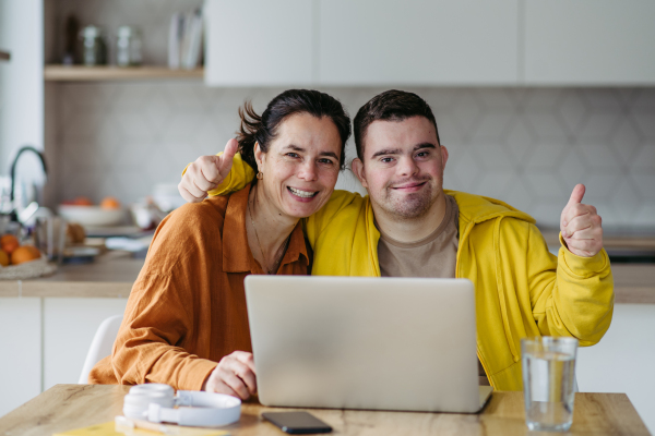 Mom teaching a young man with down syndrome, using laptop. Telehealth consultation with doctor.