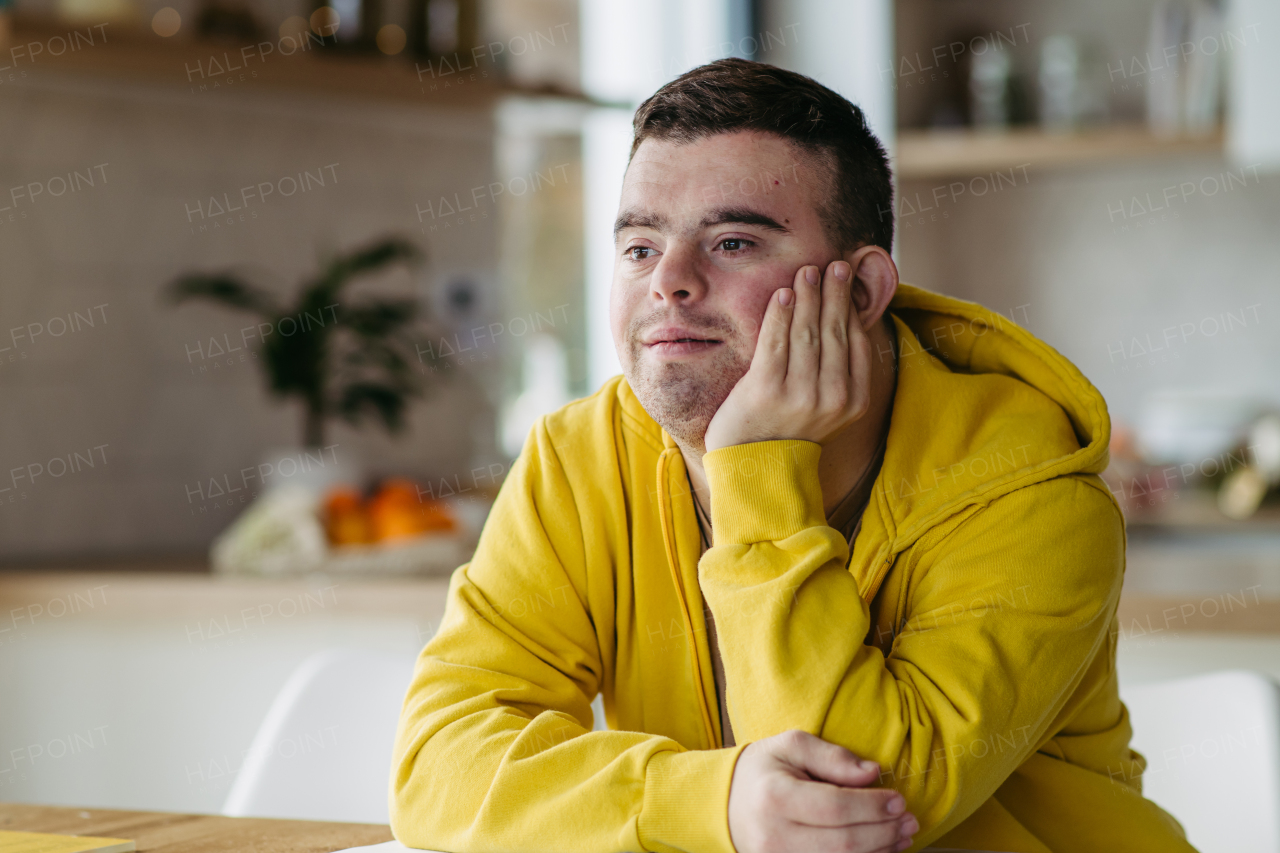 Young man with Down syndrome in kitchen, propping head up with his hand, smiling.