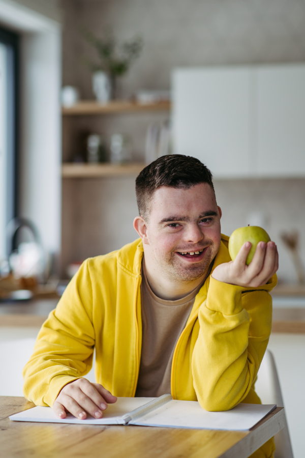 Portrait of young man with Down syndrome holding apple, sitting at the table.