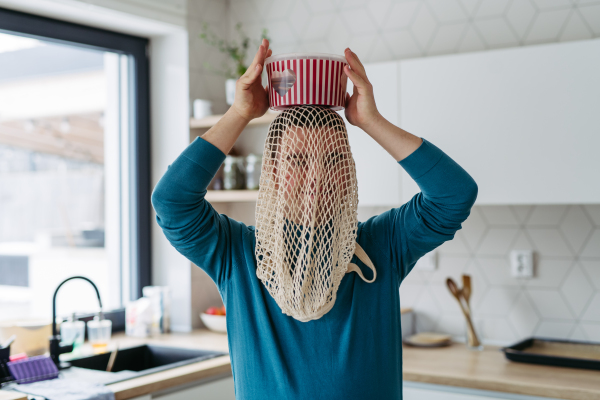 Portrait of young man with Down syndrome being funny, have mash net bag on head, holding popcorn bucket.