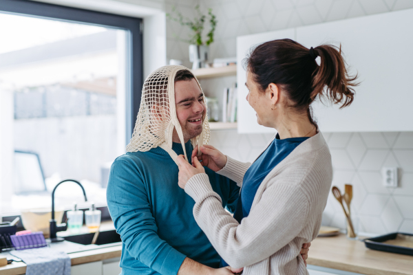 Young man with Down syndrome and his mom being funny, have mash net bag on head. Concept of love and parenting disabled child.