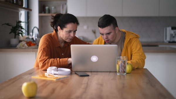 Mom teaching a young man with down syndrome, using laptop. Telehealth consultation with doctor.