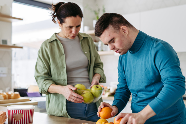 Young man with Down syndrome preparing breakfast with his mother at home. Morning routine for man with Down syndrome genetic disorder.