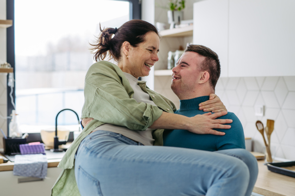 Portrait of young man with Down syndrome holding his mother in hands, looking at each other. Concept of love and parenting disabled child. Banner with copyspace.