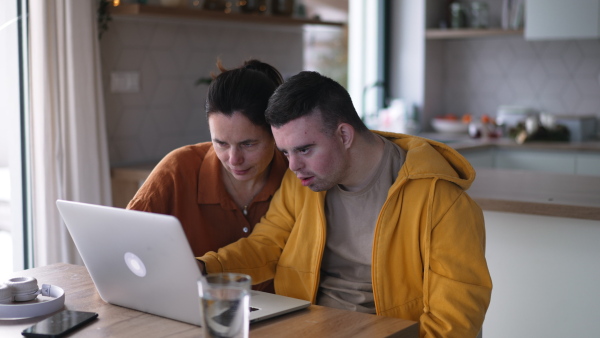 Mom teaching a young man with down syndrome, using laptop. Telehealth consultation with doctor.