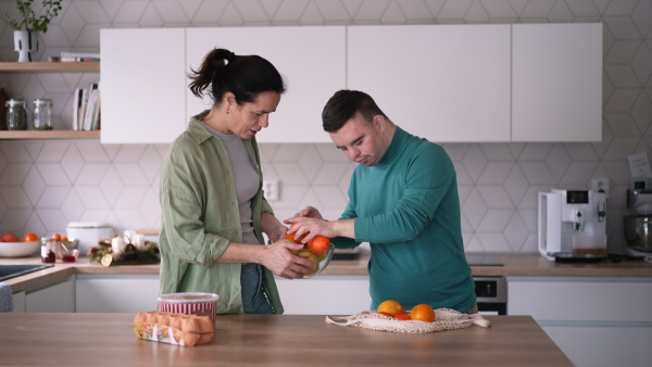 Young man with Down syndrome preparing breakfast with his mother at home. Morning routine for man with Down syndrome genetic disorder.