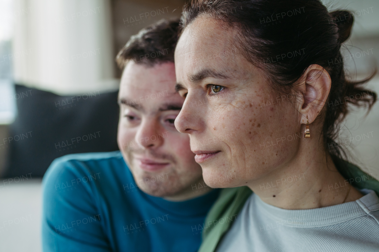 Portrait of young man with Down syndrome with his mother at home, holding, touching with foreheads. Concept of love and parenting disabled child.