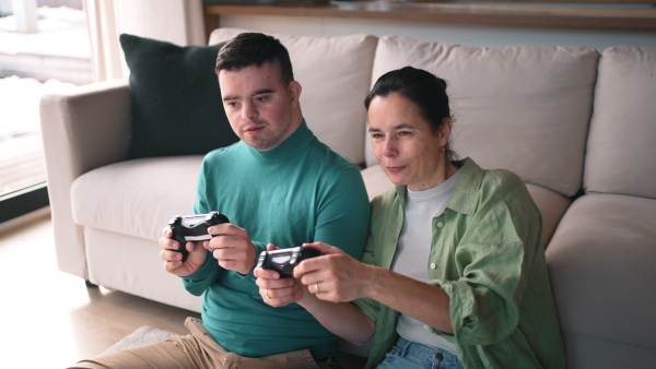 A video of young man with Down syndrome playing games on console with his mother at home.