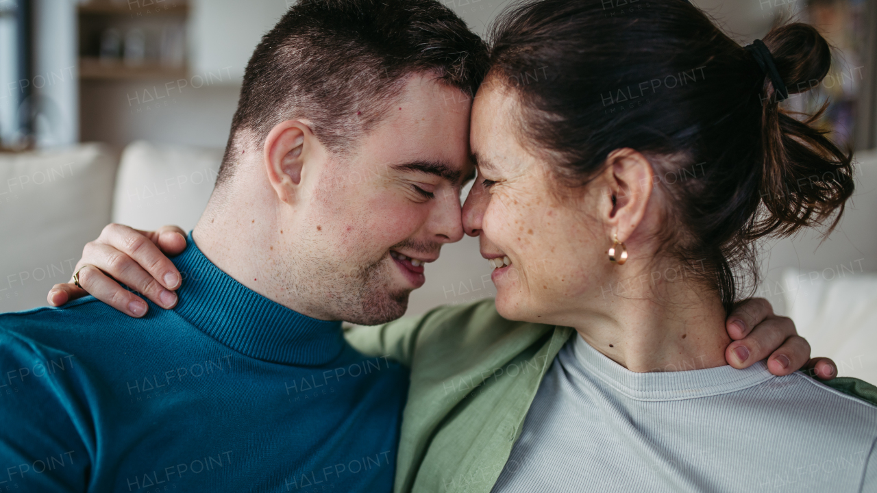 Portrait of young man with Down syndrome with his mother at home, toasting with juice. Morning routine for man with Down syndrome genetic disorder.