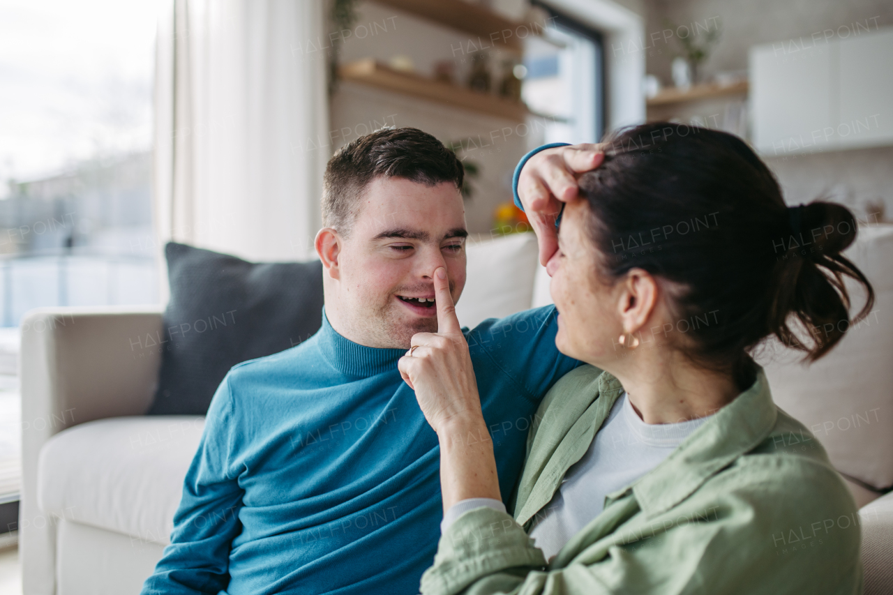 Portrait of young man with Down syndrome with his mother at home, boop on nose with finger. Morning routine for man with Down syndrome genetic disorder.