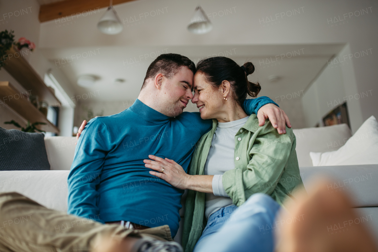 Portrait of young man with Down syndrome with his mother at home, toasting with juice. Morning routine for man with Down syndrome genetic disorder.