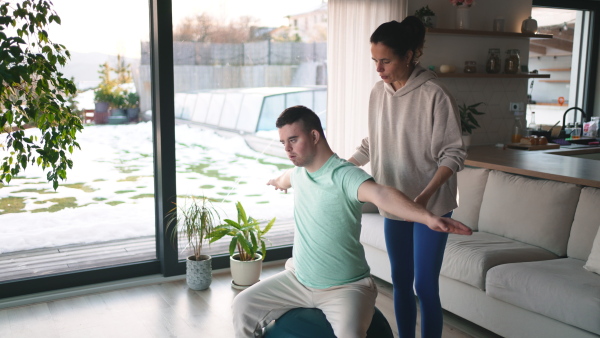 A young man with Down syndrome exercising at home with his mother. Workout routine for disabled man.