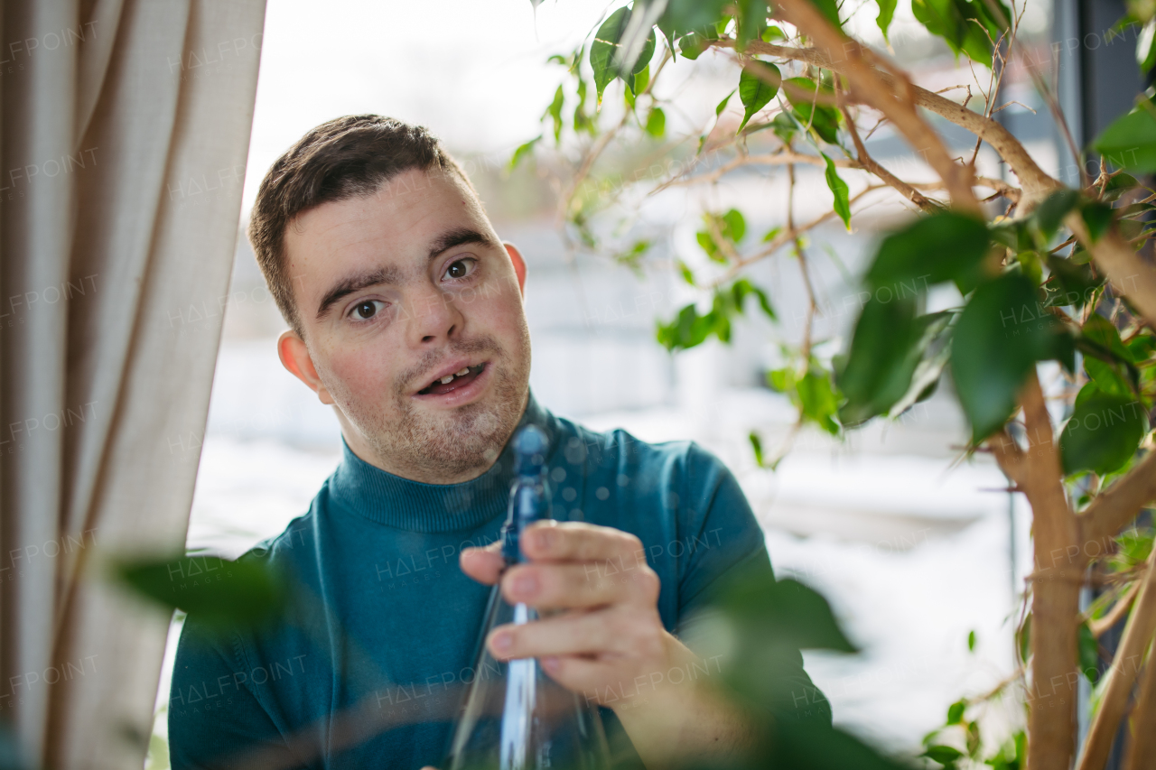 Young man with Down syndrome taking care of indoor plants, misting, spraying leaves with spray bottle.