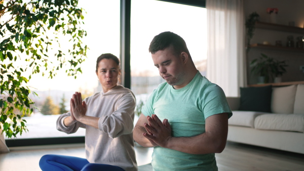 Young man with Down syndrome exercising at home with his mother. Workout routine for disabled man.