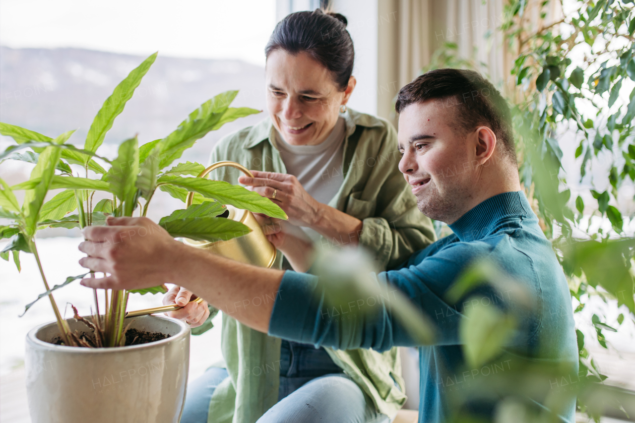 Top view of young man with Down syndrome with his mother at home, taking care of houseplants. Concept of love and parenting disabled child.