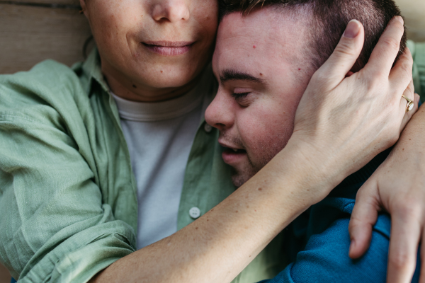 Portrait of young man with Down syndrome with his mother at home, holding, touching with foreheads. Concept of love and parenting disabled child. Close up shot.