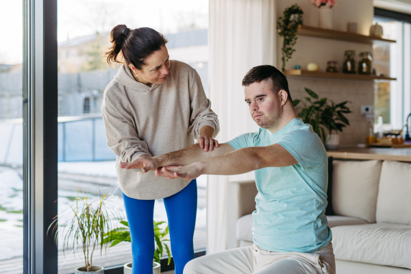 Young man with Down syndrome exercising at home with his mother. Workout routine for disabled man.