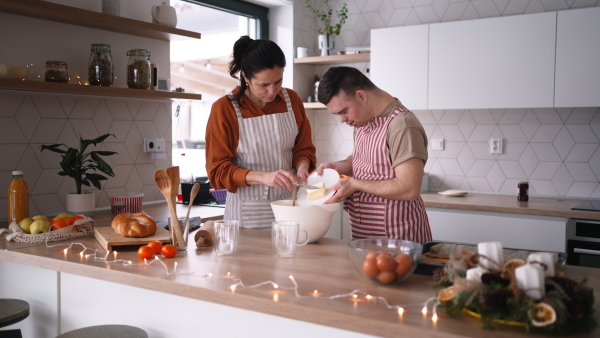 A young man with Down syndrome preparig dough for cookies with his mom at home. Everyday routine for man with Down syndrome.