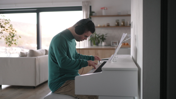 Young man with down syndrome playing on piano, listening his music via headphones. Practicing piano with headphones