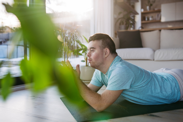 Young man with Down syndrome exercising at home, doing yoga or meditating. Man is praying, lying on belly.