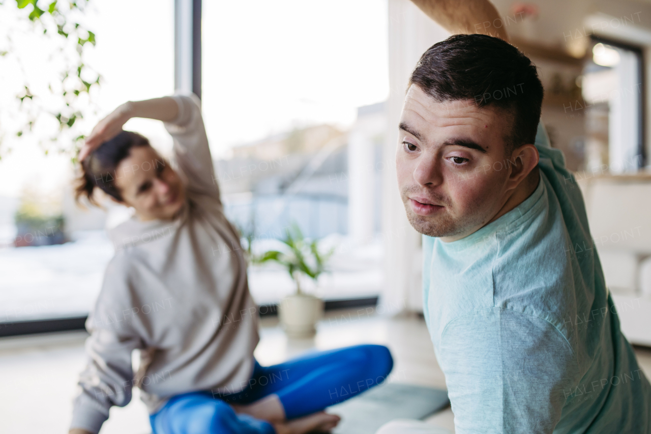 Young man with Down syndrome exercising at home with his mother. Workout routine for disabled man.