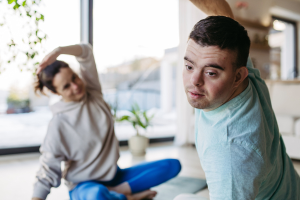 Young man with Down syndrome exercising at home with his mother. Workout routine for disabled man.